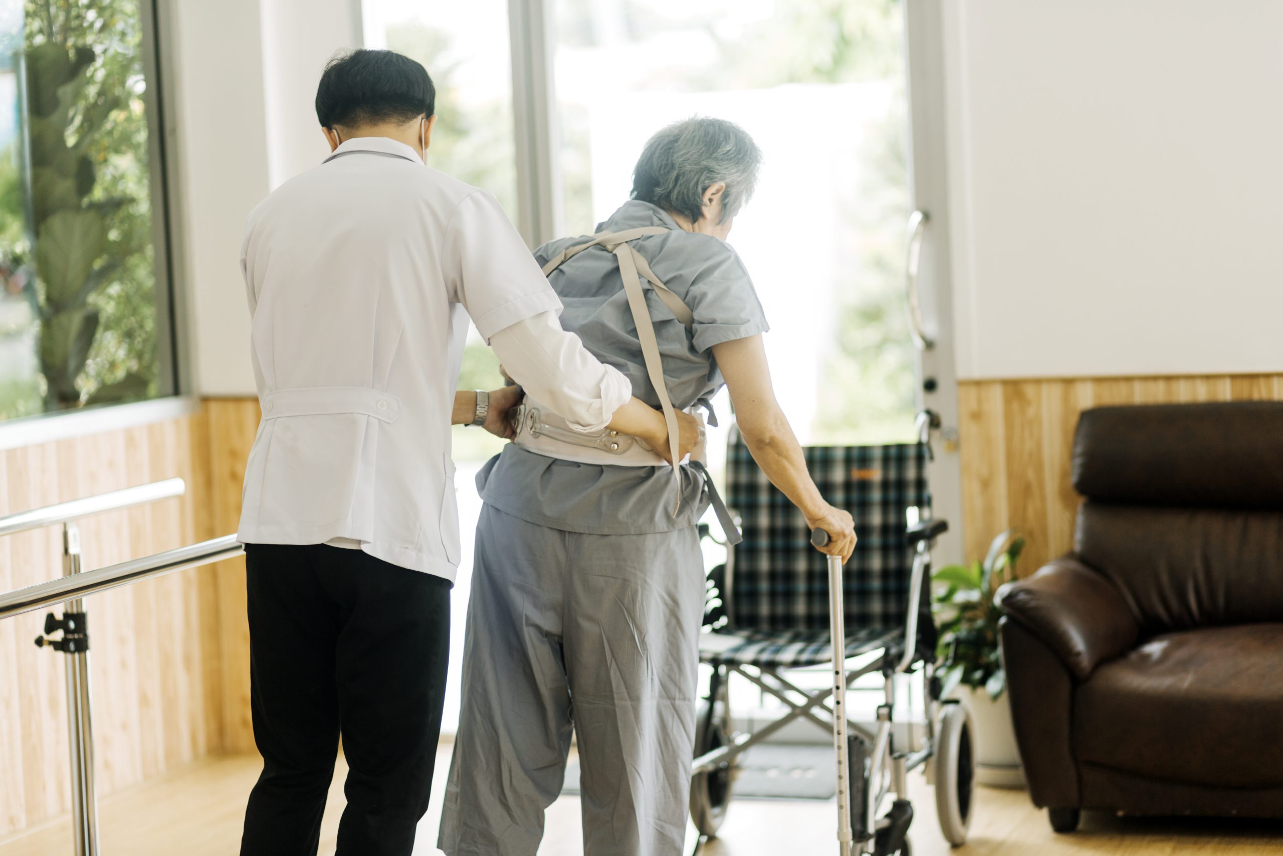 Un fisioterapeuta joven ayuda a un anciano a caminar con un andador en el pasillo de una residencia de ancianos